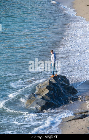 Un jeune homme debout sur les rochers à marée montante sur la petite plage de Fistral Newquay en Cornouailles. Banque D'Images