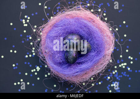 Image en arrière-plan de la galaxie-comme les oeufs de Pâques peints couché dans nid de paille de couleur sur la table en néon, voir ci-dessus Banque D'Images