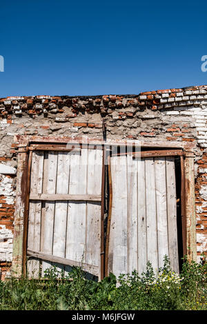 Abandonné le vieux abri de vache de mur de briques altérées et avec une porte en bois délabrée le jour ensoleillé dans la campagne Banque D'Images