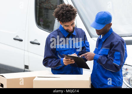 Delivery Man écrit sur le Presse-papiers sur les boîtes de carton debout près du chariot Banque D'Images