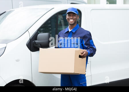 Delivery Man debout près du Van Holding Cardboard Box Banque D'Images