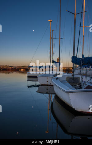 Les petits voiliers flottant dans le calme Marina Cove comme l'aube sous la pleine lune. Banque D'Images