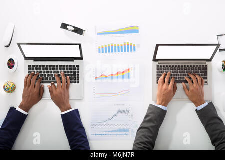 High Angle View of Two Businesspeople Using Laptop avec graphiques de bureau Banque D'Images