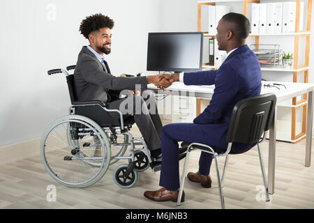 Deux hommes d'heureux assis sur fauteuil roulant et président en serrant la main avant de l'ordinateur Banque D'Images