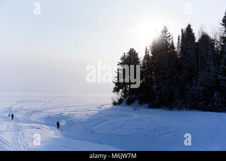 La bouche recouverte de glace d'une rivière qui coule d'hiver dans un lac, dans une brume glaciale, avec une haute rive et personnes marchant sur la glace Banque D'Images