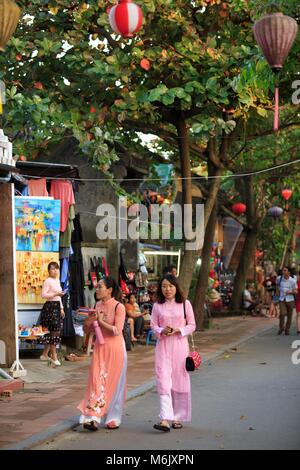 Deux femmes en vêtements traditionnels Ao Dai shopping dans les rues de Hoi An, Vietnam Banque D'Images