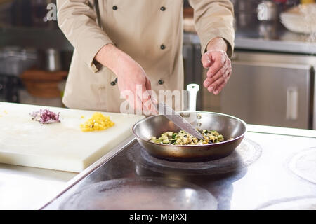 Chef cooking les légumes dans une poêle. Banque D'Images