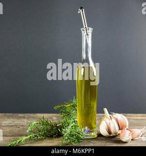 La bouteille sur la table en bois contient de l'huile d'olive extra vierge produite en Italie. L'ail et le romarin sont les herbes aromatiques Banque D'Images