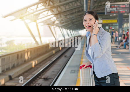 Happy Young Asian businesswoman talking on the phone avec son client et sur la plate-forme de voir le train venant de son voyage réunion. Banque D'Images