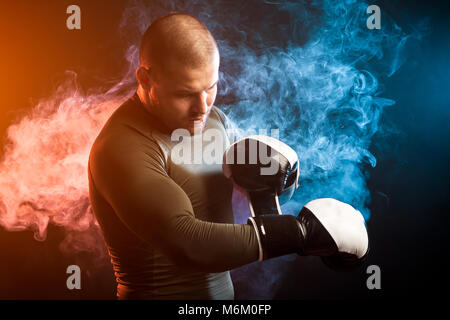 Un jeune athlète masculin brune dans une veste de sport vert posant et portant des gants de boxe noir et blanc sur fond de bleu et rouge Banque D'Images