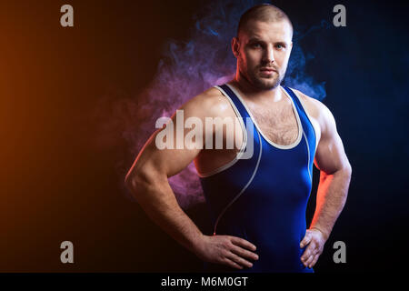 Un jeune homme dans un lutteur sportif sports shirt vert et bleu wrestling-stands et avec confiance garde ses mains sur la taille contre un et bleu Banque D'Images