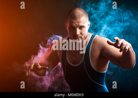 Un solide brun velo dans un collant bleu wrestling posant contre un rouge et bleu sur un fond de fumée vape isolé noir Banque D'Images