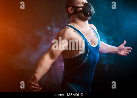 Un solide brun velo dans un collant bleu et de formation de lutte contre une pose de masque rouge et bleu sur un fond de fumée vape isolé noir Banque D'Images