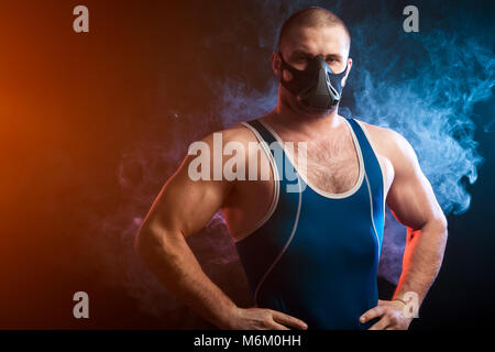 Un solide brun velo dans un collant bleu et de formation de lutte contre une pose de masque rouge et bleu sur un fond de fumée vape isolé noir Banque D'Images