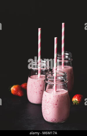 Les smoothies fraises fraîches dans des bocaux avec paille rose sur fond sombre, selective focus et copie espace pour le texte. Mode de vie sain, fitness, d Banque D'Images