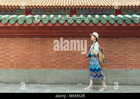 Balades touristiques heureux passé le mur de brique rouge du temple de Confucius sur l'Asie au cours de l'été voyage en Chine. Jeune femme portant tenue d'été et la tenue d'un Banque D'Images