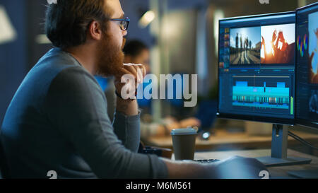 Éditeur vidéo mâle fonctionne avec des images et de son sur son ordinateur personnel avec deux écrans. Il travaille dans un bureau Cool Loft avec d'autres personnes créatives. Banque D'Images