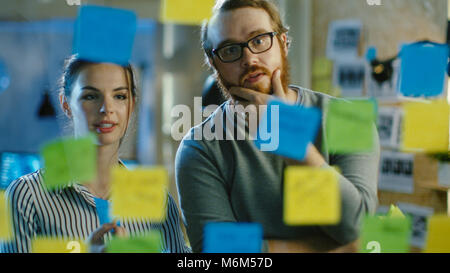 Homme et femme Les concepteurs et leur prochain projet sur un mur de verre avec des notes adhésives Contour. Ils sont jeunes et créatifs qui travaillent dans un office de tourisme Banque D'Images