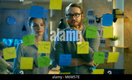 Homme et femme Les concepteurs et leur prochain projet sur un mur de verre avec des notes adhésives Contour. Ils sont jeunes et créatifs qui travaillent dans un office de tourisme Banque D'Images