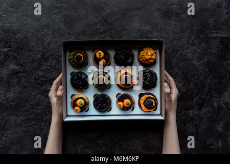 Cropped shot of human hands holding cupcakes halloween sur noir Banque D'Images