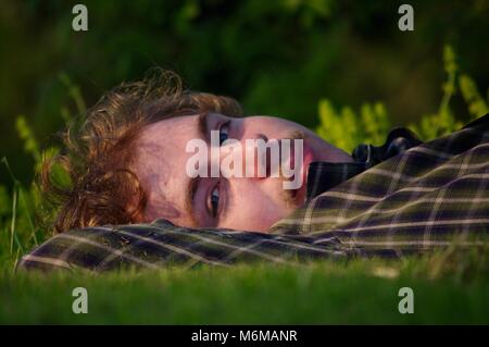 Naturaliste adolescents reposant, couchée sur l'herbe animée luxuriante de la rivière Exe, dans la lumière dorée d'un soir d'été. Exeter, Devon, UK. Banque D'Images