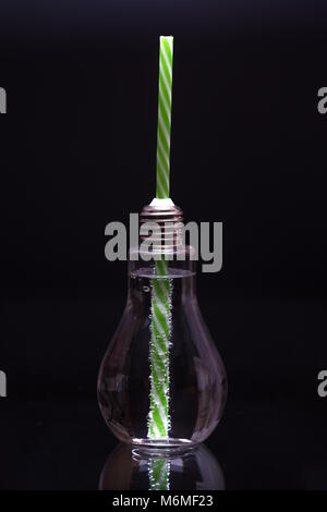 L'eau minérale en bouteille en verre avec paille isolé sur fond noir Banque D'Images