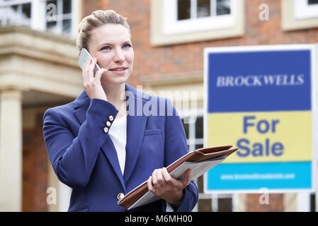 Female Realtor sur téléphone en dehors de la Propriété résidentielle à vendre Banque D'Images