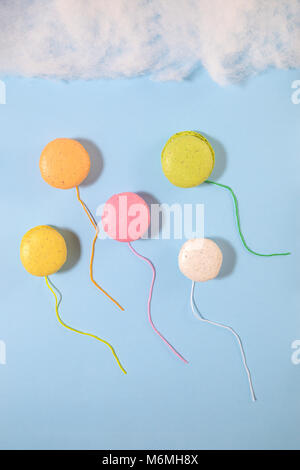 Macarons colorés en forme de ballons sur papier bleu fond ciel avec nuages de coton. Concept minimal Banque D'Images