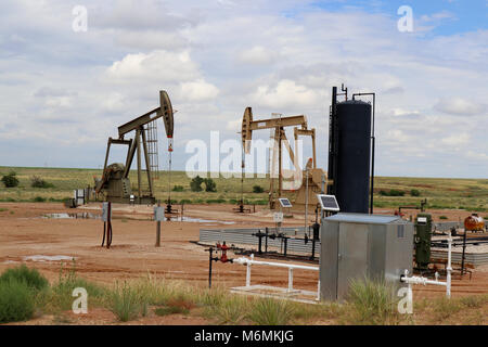 - L'huile de deux gaz pompe à balancier au site de forage avec de l'équipement et des réservoirs sur praries avec basse colline derrière et blue cloudy sky Banque D'Images