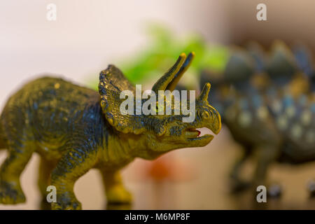 Close up photo de petit jouet Triceratops en premier plan l'accent avec toy et arbres en arrière-plan le stegosaurus hors focus Banque D'Images