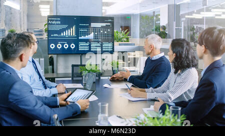 Groupe diversifié de gens d'affaires dans la salle de conférence, discuter de la croissance de l'entreprise indiqué sur le mur plat illustré par des graphiques et statistiques Banque D'Images