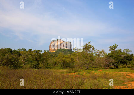 Sigiriya Rock historique au Sri Lanka avec bois et de frotter sur le sol de sable rouge bleu sous un ciel nuageux Banque D'Images