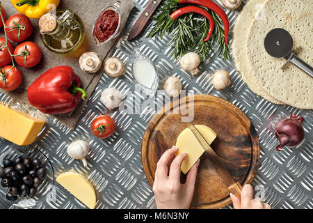 Vue partielle de la femme la découpe du fromage pendant la cuisson de la pizza italienne maison Banque D'Images