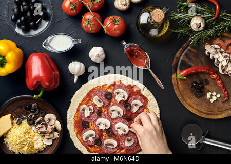 Mains de Baker l'ajout d'ingrédients dans la préparation de pizza pizza au cours de cuisine à Banque D'Images