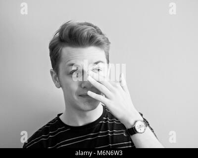 1960 Style : Noir et blanc portrait of young man. Il se gratta l'arrête du nez. Banque D'Images