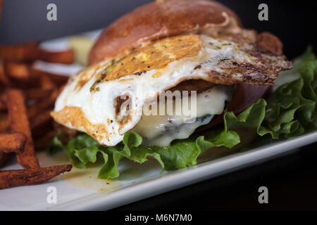 Hamburger plaqué avec dressing, la laitue et un œuf frit dans un petit pain croustillant et frites de patates douces sur le côté Banque D'Images