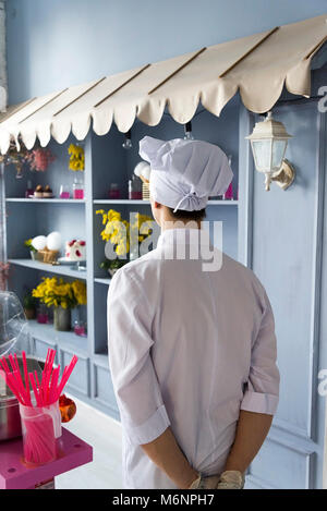 Vue arrière du chef dans la cuisine du restaurant. Dans une robe blanche et un chapeau. Banque D'Images