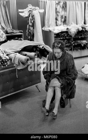 Femme âgée d'âge moyen à la mode faisant du shopping, assise pieds fatigués. Elle porte un vrai manteau de fourrure dans le département tissu d'un grand magasin londonien Londres UK 1971 1970s. HOMER SYKES Banque D'Images