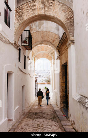 Un couple de touristes à pied à travers une ruelle à arcades typiques de Vejer de la Frontera, province de Cadiz, Andalousie, Espagne Banque D'Images
