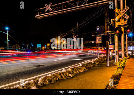 Le trafic passant traverser les voies de chemin de fer sur une route très fréquentée à l'heure de pointe. Feux clignotants et d'inhibition des voitures quand train passe avec les banlieusards de nuit Banque D'Images