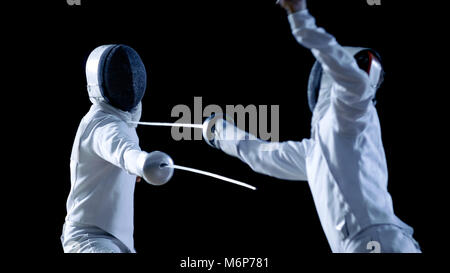 Deux tireurs professionnels montrent de l'Épée de Maître dans leur lutte d'aluminium. Ils attaquent, défendre, Leap et de poussée et sur une jambe. Shot isolated on Black Banque D'Images