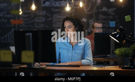 Belle femme Employé de bureau travaille à son bureau sur un ordinateur personnel. Dans l'arrière-plan à un collègue dans le bureau de création. Banque D'Images