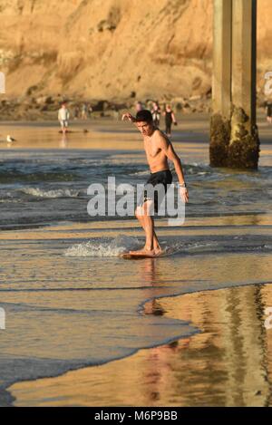 Jeune homme sur une board, un survol, à la plage pendant le coucher du soleil et glissent sur les vagues, San Diego, Californie, USA. Banque D'Images