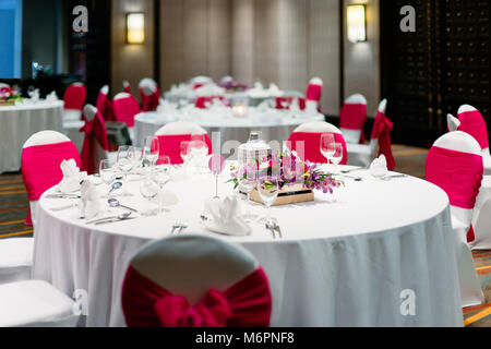 La réception de mariage décoration de table de dîner avec des orchidées, des fleurs, des bougies, des chaises spandex blanc couvercle avec ceinture organza rouge Banque D'Images