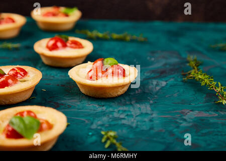 Mini tartelettes aux tomates cerises de fromage mozzarella sur fond vert. Banque D'Images