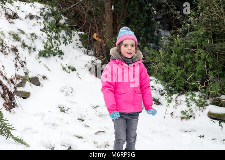 Cute little girl standing dans la neige portant veste rose et bleu pompom hiver hat Banque D'Images