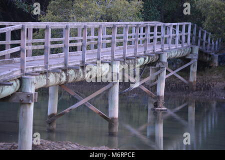 Scène pastel, image au crépuscule d'une passerelle en bois décolorée sur des poteaux en bois ronds se reflétant dans creek à Moonee Beach, Nouvelle-Galles du Sud, Australie Banque D'Images