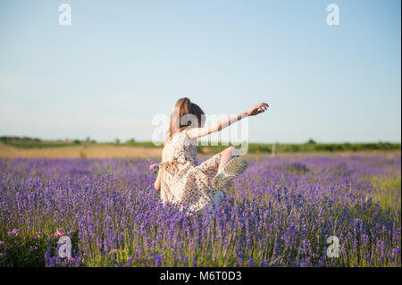 Petite fille mince robe en hauteur traverse les buissons dans le domaine parmi les fleurs de lavande Banque D'Images