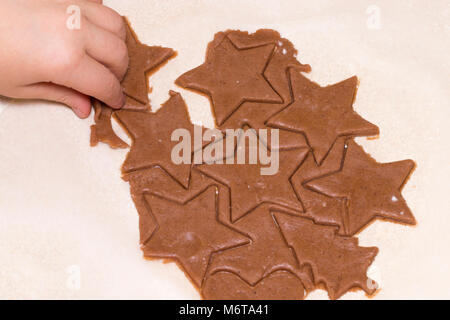 Kid mains cut cookie à partir de pâte crue sur une table en bois. Les biscuits de Noël et de l'alimentation de concept. Banque D'Images