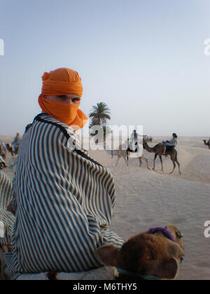 Un homme portant des vêtements traditionnels tunisiens est monté sur un chameau dans le désert du Sahara Banque D'Images